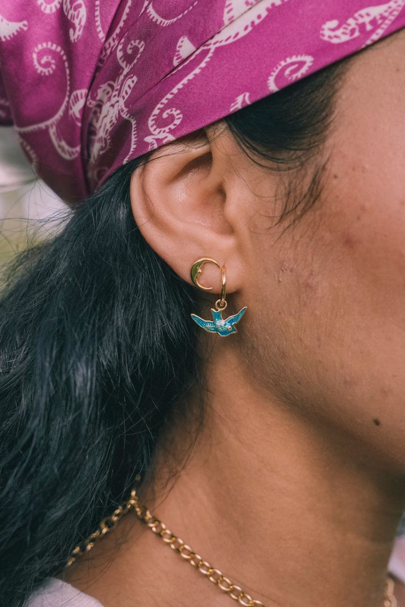 Close-up of a person wearing a gold hoop earring with a blue pendant, purple headscarf, and gold necklace.